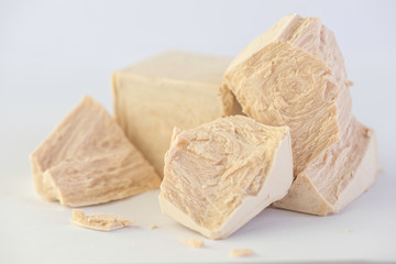 cube of fresh yeast whole and crumbled on a white background 