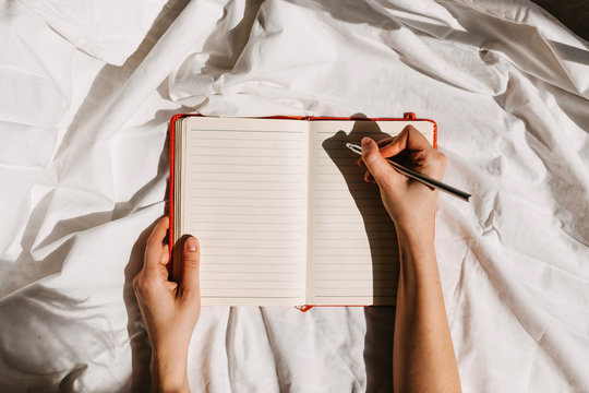 Hands holding an open blank notebook and a pen on bed background.
