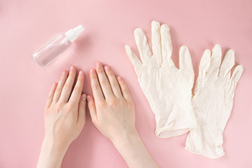 Female hands, sanitizer spray bottle and rubber gloves flat lay on pink background top view. Disinfecting hands for coronavirus protetcion, personal hygiene, virus prevetion. Web banner. Stock photo.