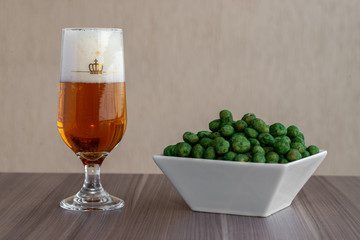Copo de cerveja sem marca com enfeite de coroa dourado, cerveja pilsen com amendoim verde de cebola...