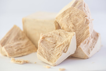 cube of fresh yeast whole and crumbled on a white background 