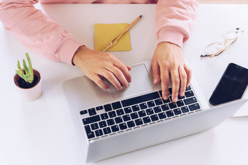 Woman hands working at laptop on a white marble desk.