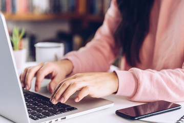 Young woman working at laptop on white marble desk at her home.
