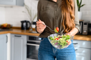 A bowl of fresh salad in the hands of a woman close-up, a tomato on a fork. The face is not visible. Vegetarian food