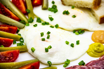 Delicious breakfast with eggs, salami, cucumbers, cherry tomatoes, slices of loaf, sauces and green onion on top on a white plate. Healthy and tasty meal for breakfast or lunch.