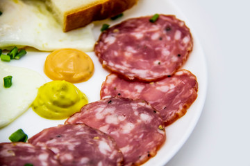 Delicious breakfast with eggs, salami,  slices of loaf, sauces and green onion on top on a white plate. Healthy and tasty meal for breakfast or lunch.