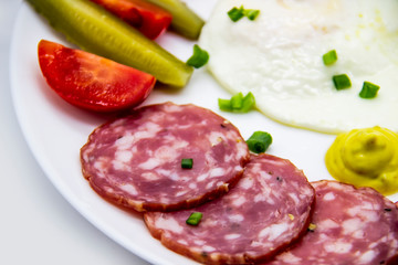 Delicious breakfast with eggs, salami, cucumbers, cherry tomatoes, sauces and green onion on top on a white plate. Healthy and tasty meal for breakfast or lunch.