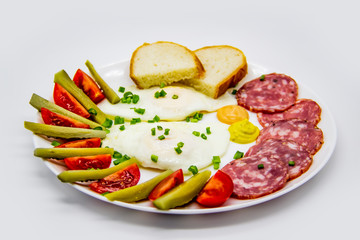 Delicious breakfast with eggs, salami, cucumbers, cherry tomatoes, slices of loaf, sauces and green onion on top on a white plate. Healthy and tasty meal for breakfast or lunch.