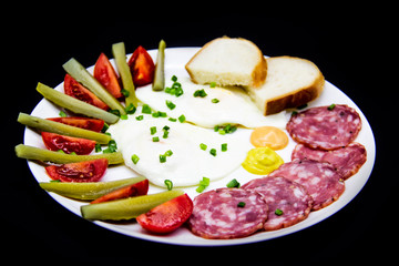 Delicious breakfast with eggs, salami, cucumbers, cherry tomatoes, slices of loaf, sauces and green onion on top on a white plate. Healthy and tasty meal for breakfast or lunch.