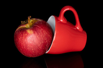 One whole fresh garden apple with red cup isolated on black glass