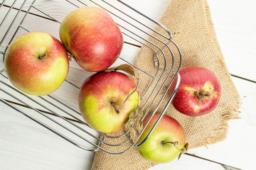 Group of five whole fresh garden apple in basket on jute cloth on white wood