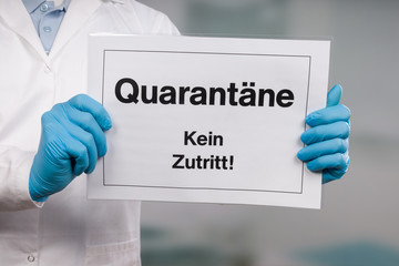Doctor's hand in medical gloves showing german quarantine sign in front of a restricted area