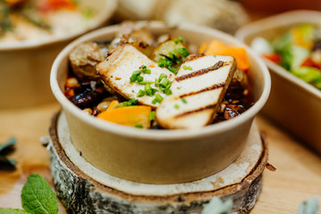 Vegetarian and vitamin-rich dish with tofu, beans and potatoes in eco-box, delivered by a delivery service, ordered online, decorated with bundles of straw on white wood, all in a Mediterranean style