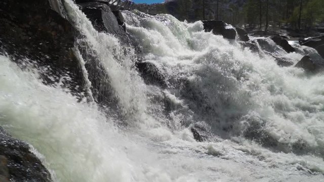 A slow-motion video of the powerful Gaula river at the Likholefossen waterfall. A mass of water falling from the rocks, whirling, foaming and splashing around. Water spray hanging in the air.