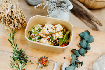 Vitamin-rich vegan food with tofu, couscous, paprika and mushrooms in eco box delivered by a delivery service, ordered online, decorated with rosemary on a wooden surface, all in a Mediterranean style