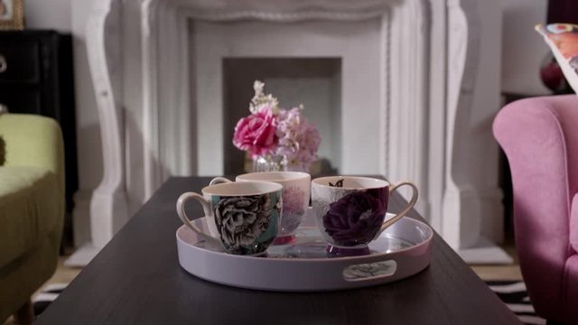 Tilt down from an ornate fireplace to a coffee table with a tray of floral teacups, full and waiting for an afternoon visit.