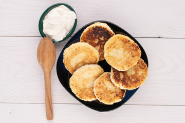 Group of six whole cheese pancake with sour cream on white wood