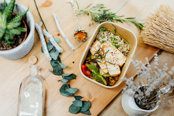 Vitamin-rich vegan food with tofu, couscous, paprika and mushrooms in eco box delivered by a delivery service, ordered online, decorated with rosemary on a wooden surface, all in a Mediterranean style