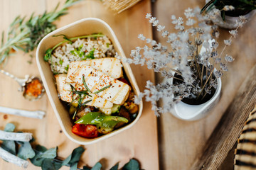Vitamin-rich vegan food with tofu, couscous, paprika and mushrooms in eco box delivered by a delivery service, ordered online, decorated with rosemary on a wooden surface, all in a Mediterranean style