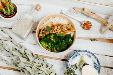 high protein food with broccholi, chicken breast, rice and aubergine in eco box delivered by a delivery service, ordered online, decorated with dried mint and spices on white wood