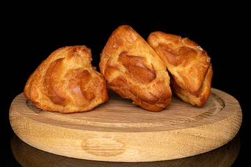 Group of three whole fresh baked profiterole on wooden plate isolated on black glass