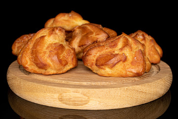 Group of five whole fresh baked profiterole on wooden plate isolated on black glass