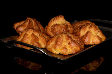Group of five whole fresh baked profiterole on tray isolated on black glass