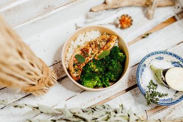 high protein food with broccholi, chicken breast, rice and aubergine in eco box delivered by a delivery service, ordered online, decorated with dried mint and spices on white wood