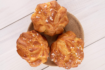Group of three whole fresh baked profiterole on ceramic plate on white wood
