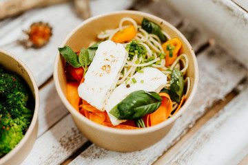 Protein-rich food with halloumi, pasta, peppers and carrots in eco box delivered by a delivery service, ordered online, decorated with basil and spices on a white wooden surface