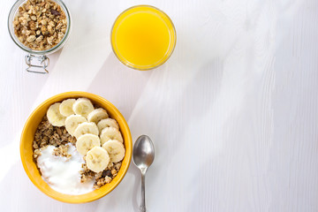Healthy breakfast of muesli with banana and yogurt, orange juice on a white wooden background