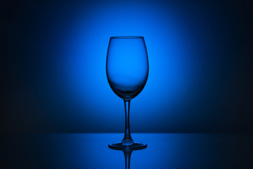 An empty glass goblet on a monochrome background with a spot of light at the back