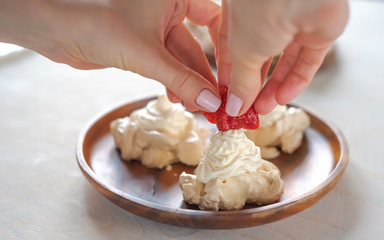 the process of creating Pavlova dessert, decorating the meringue with strawberries
