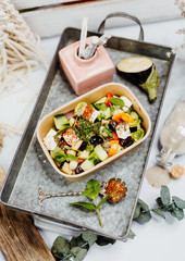 Salad rich in vitamins with olives, feta, zucchini and aubergine in eco box delivered by a delivery service, ordered online, decorated with mint and spices on a retro metal tablet