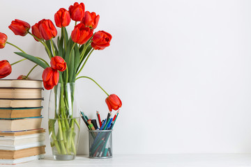 Red tulips in a vase, books and school supplies on a white background. The concept of a postcard for teacher's day. Copy space.
