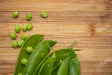 aerial macro view of opened pods with green peas on a wooden surface