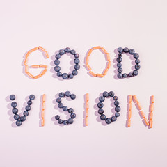 Vitamins and supplements for healthy eyes on pink background. How to maintain good vision concept. Blueberry and orange capsules forming words good vision, flat lay, top view