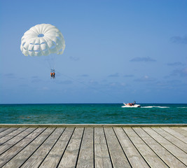 Empty wooden platform beside tropical beach at Punta Cana, Dominican Republic. White parasail wing flying over water of Sargasso Sea in the background