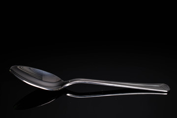 One whole steel silver spoon isolated on black glass