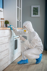 Woman in white workwear and protective gloves disinfecting the room