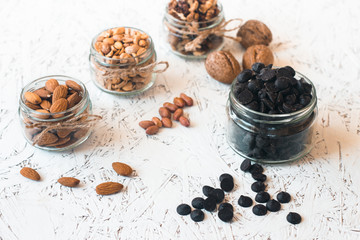 Assorted nuts in glass jars and chocolate on a white background. Vegan. Healthy eating