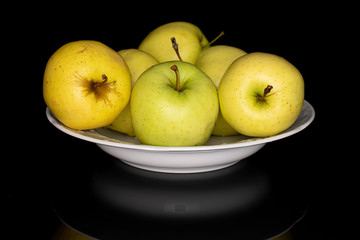 Lot of whole green delicious apple in white bowl isolated on black glass