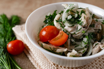 Marinated oyster mushrooms, garnished with cherry tomatoes and green dill. A dish with onions and butter in a white plate with a beige light cloth on the table