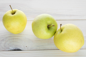 Group of three whole green delicious apple on white wood