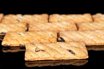 Lot of whole square puff cookie with raisins closeup isolated on black glass
