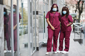 Two african american female doctors at red lab uniform in protective facial mask. Medicine, profession and healthcare concept. Stop coronavirus infection.