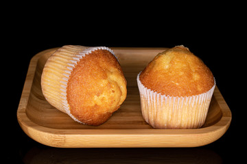 Group of two whole small baked muffin on wooden square plate isolated on black glass