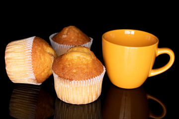 Group of three whole small baked muffin with yellow cup isolated on black glass