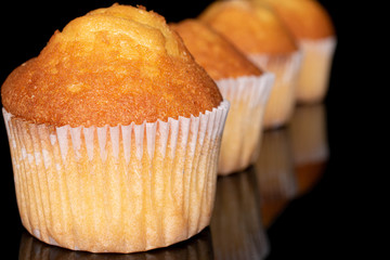 Group of four whole small baked muffin in row isolated on black glass
