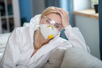Blonde woman in white workwear and respirator holding her head